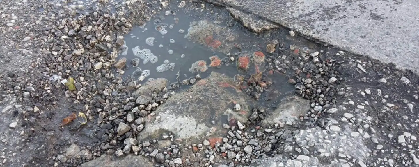 A pothole part-filled with loose stone — Pothole Repairs in Harrow by Meads Resurfacing