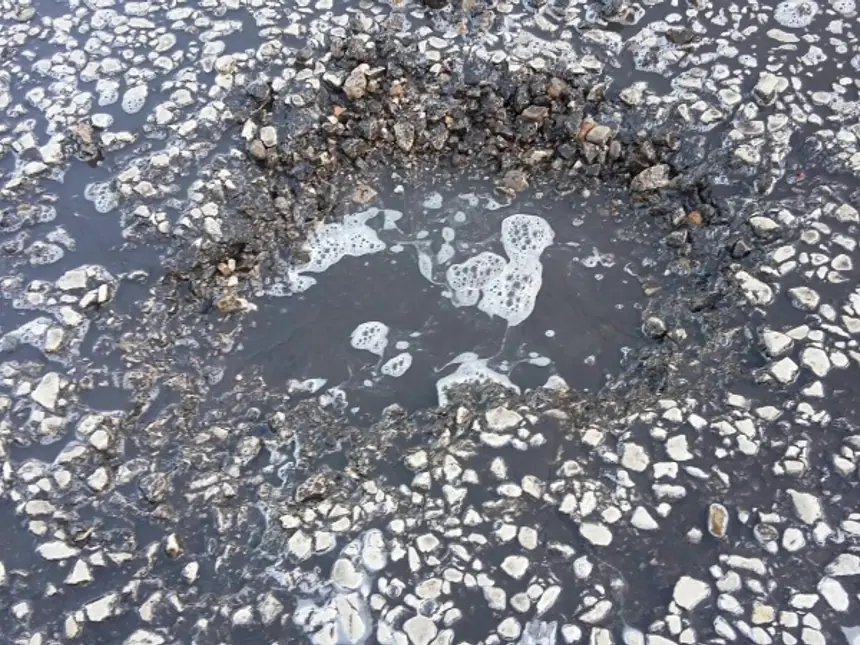A deep pothole in a worn road surface